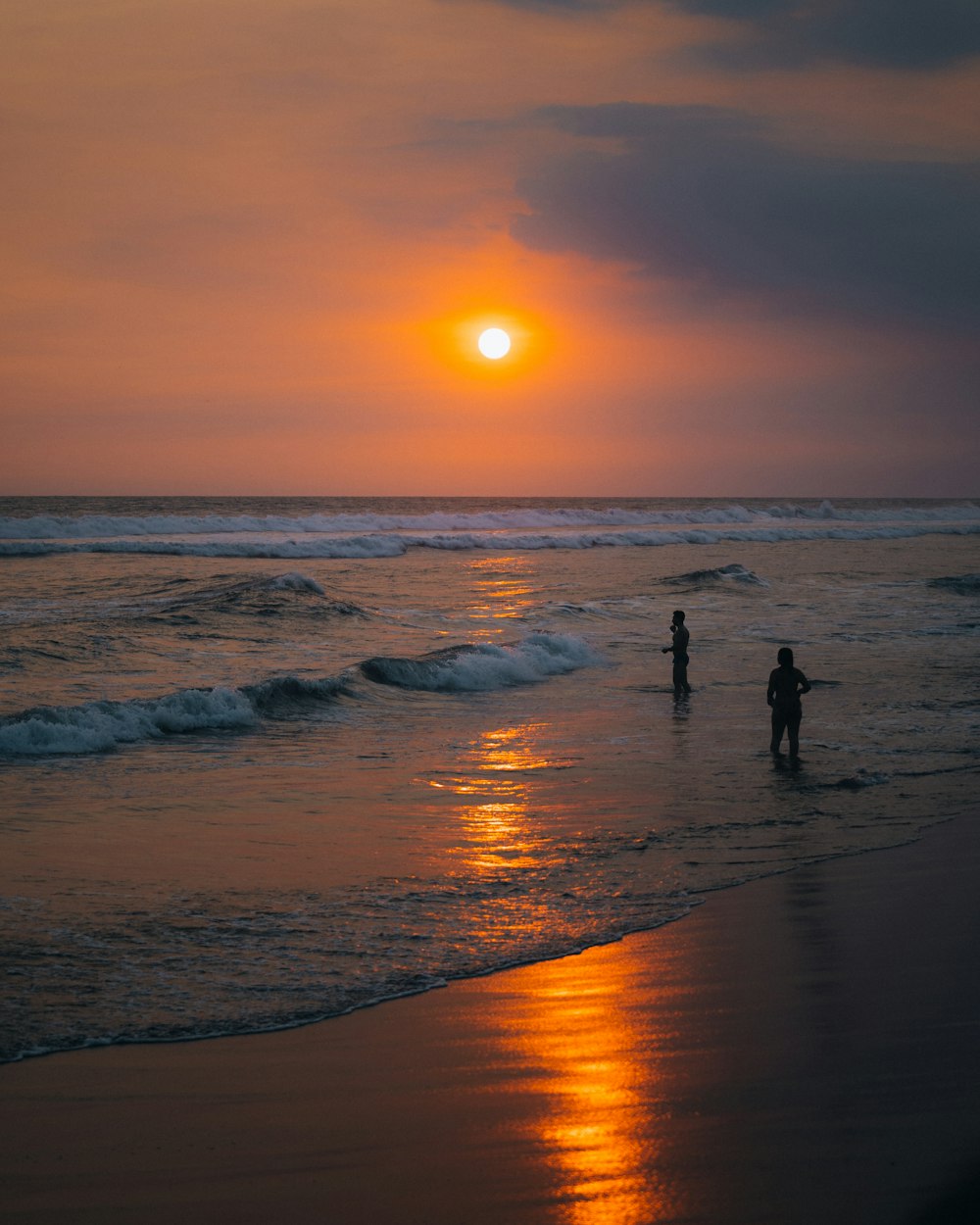 a couple of people standing on top of a beach next to the ocean