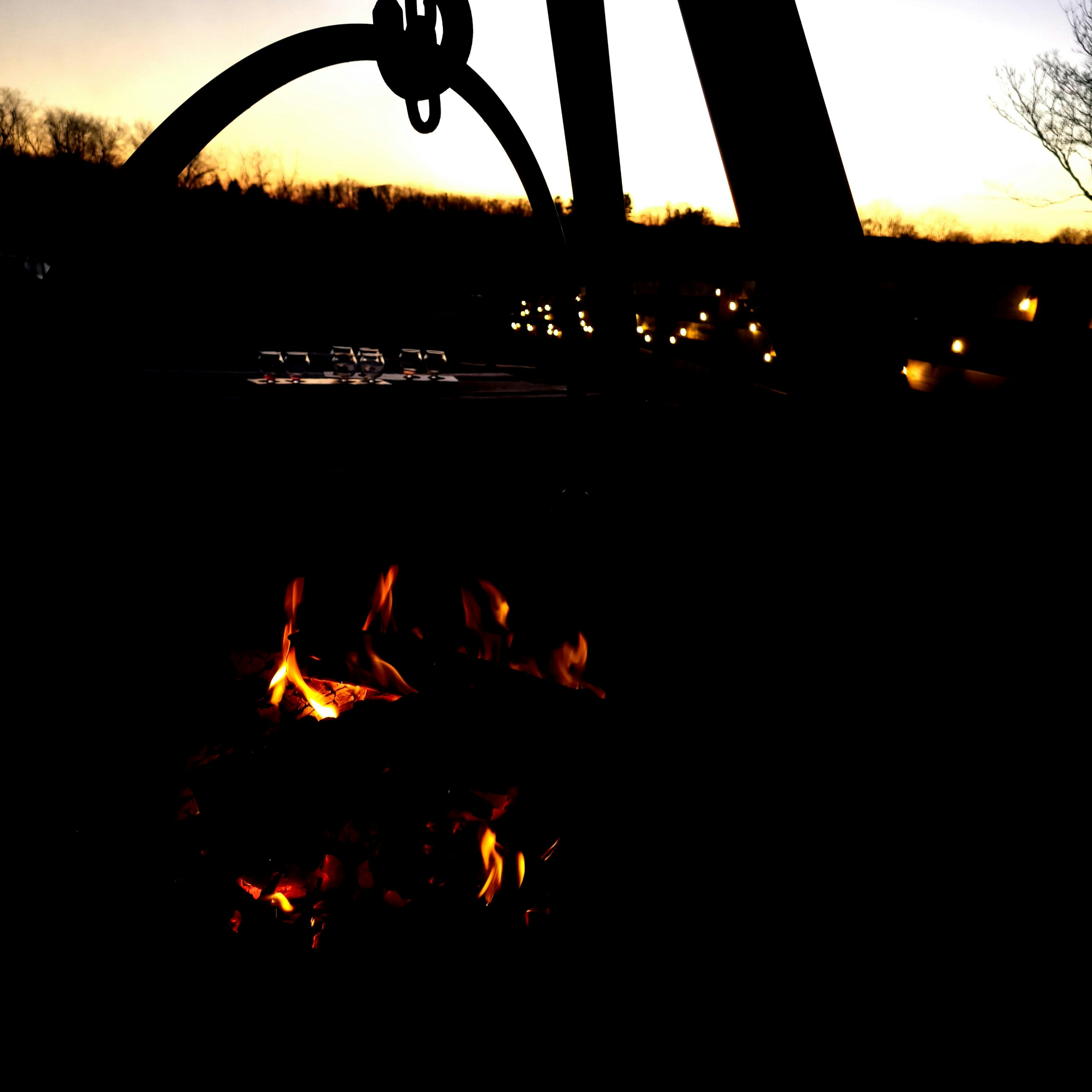 Atmospheric outdoor scene at night, deep dark sky, warm amber campfire glow, silhouetted figures, cinematic wide shot