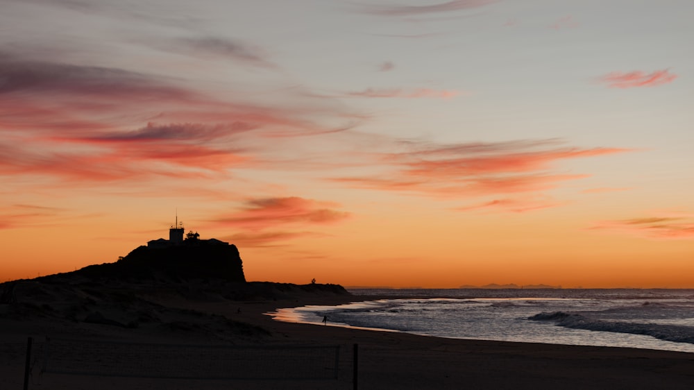 a sunset view of a beach with a lighthouse in the distance