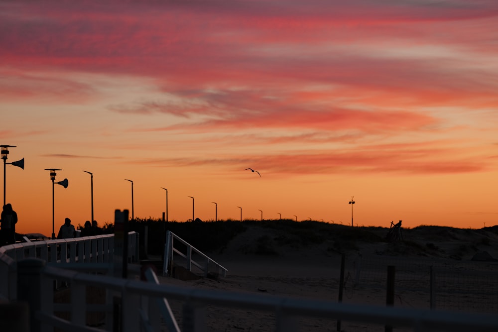 a sunset over a beach with people walking on the boardwalk