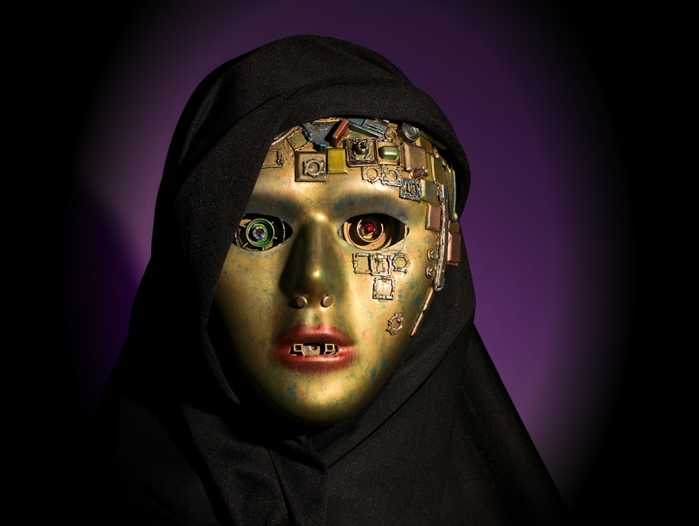 a woman wearing a gold mask and a black hood