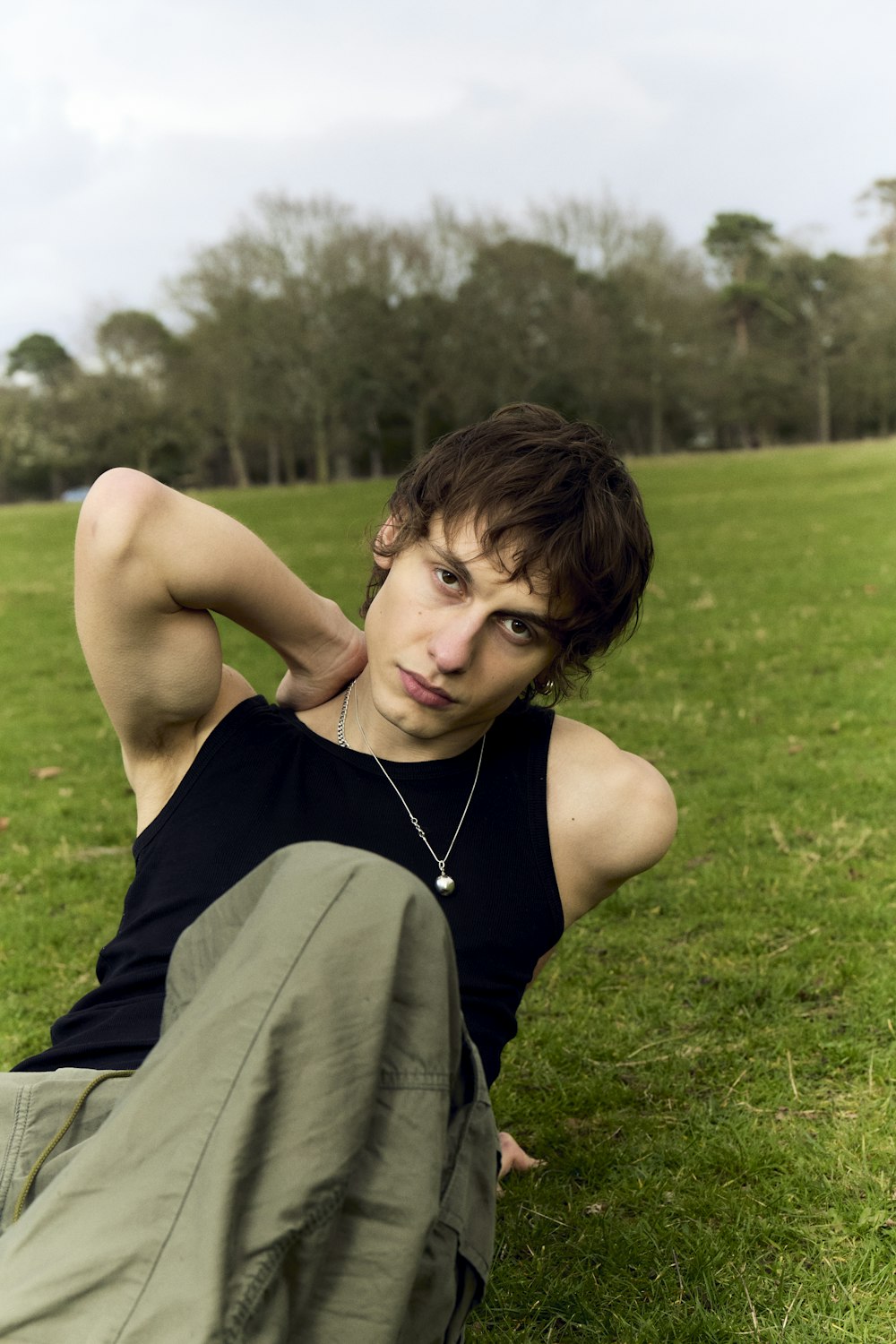a young man sitting in the grass with his hands behind his head