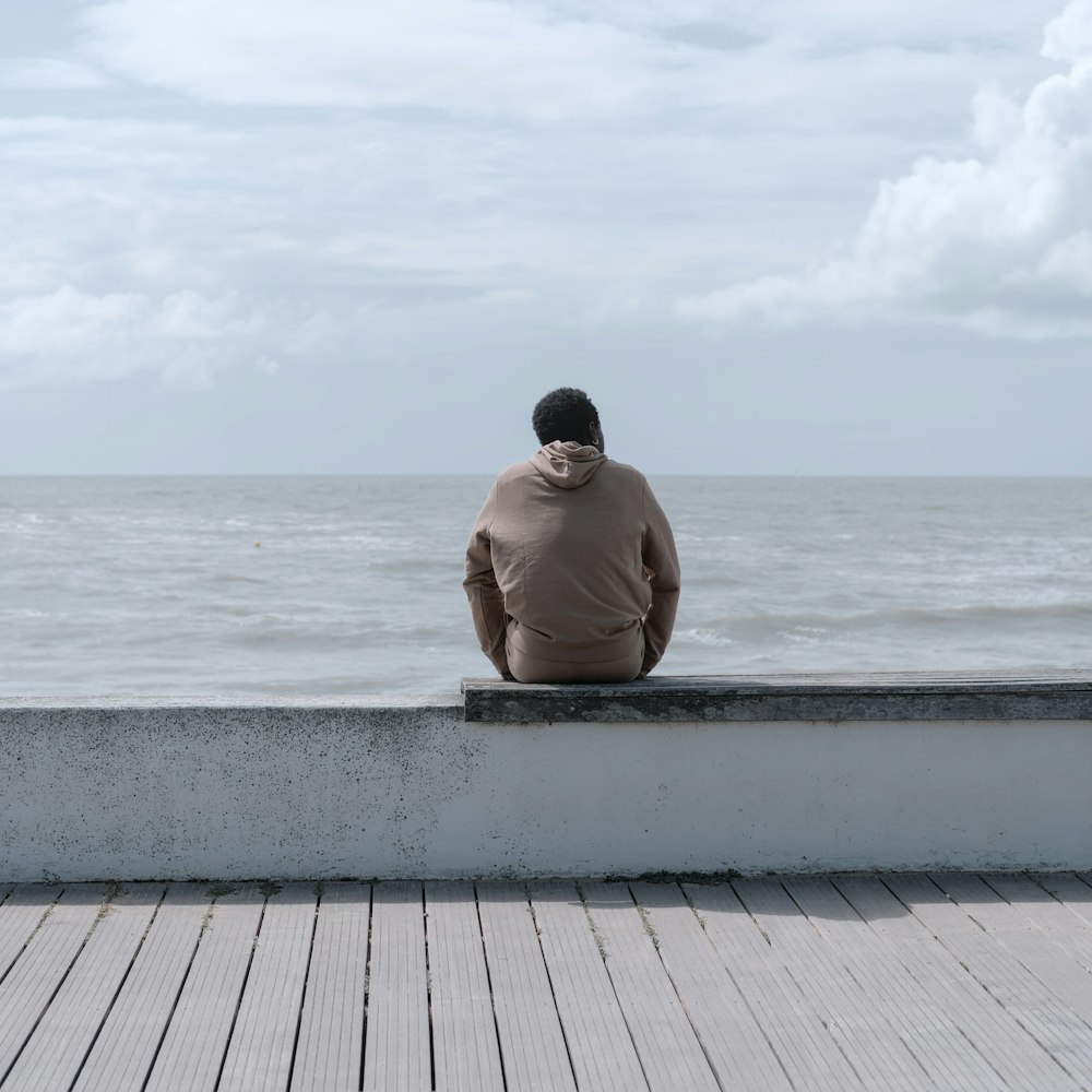 a man sitting on a ledge looking out at the ocean
