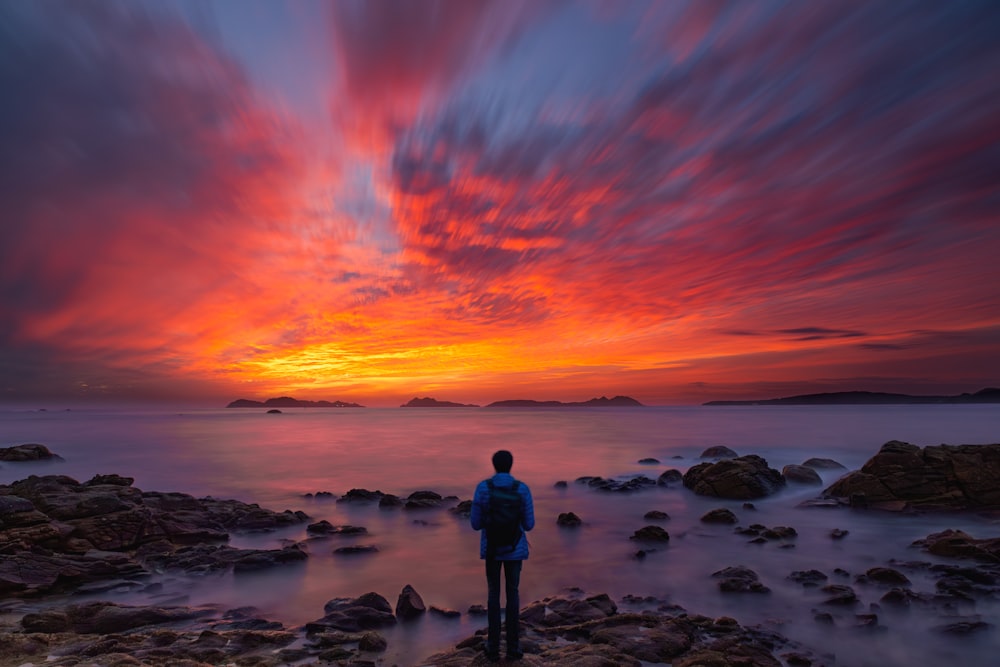 a man standing on a rocky beach at sunset