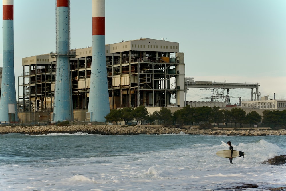 a man holding a surfboard in front of a factory