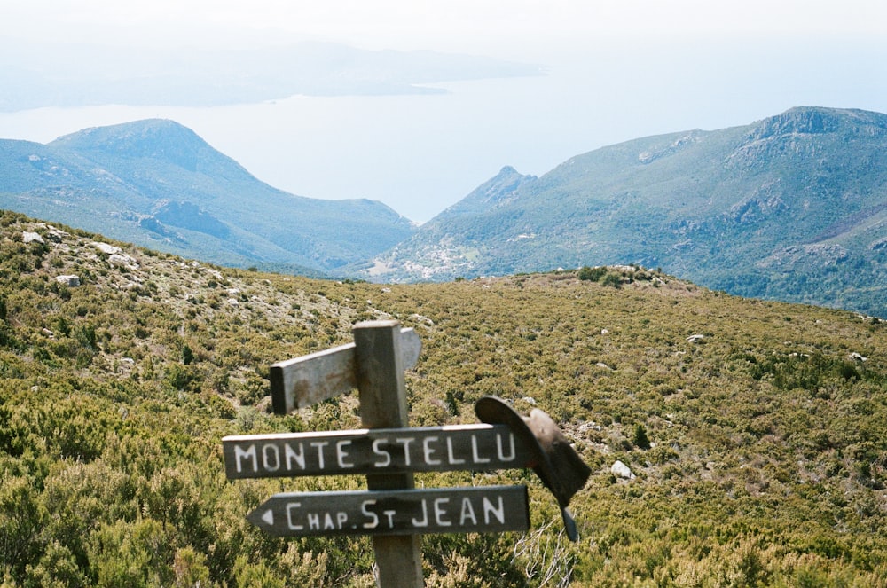 a wooden sign on a hill with mountains in the background