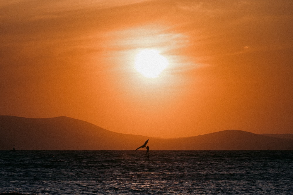 a person windsurfing in the ocean at sunset