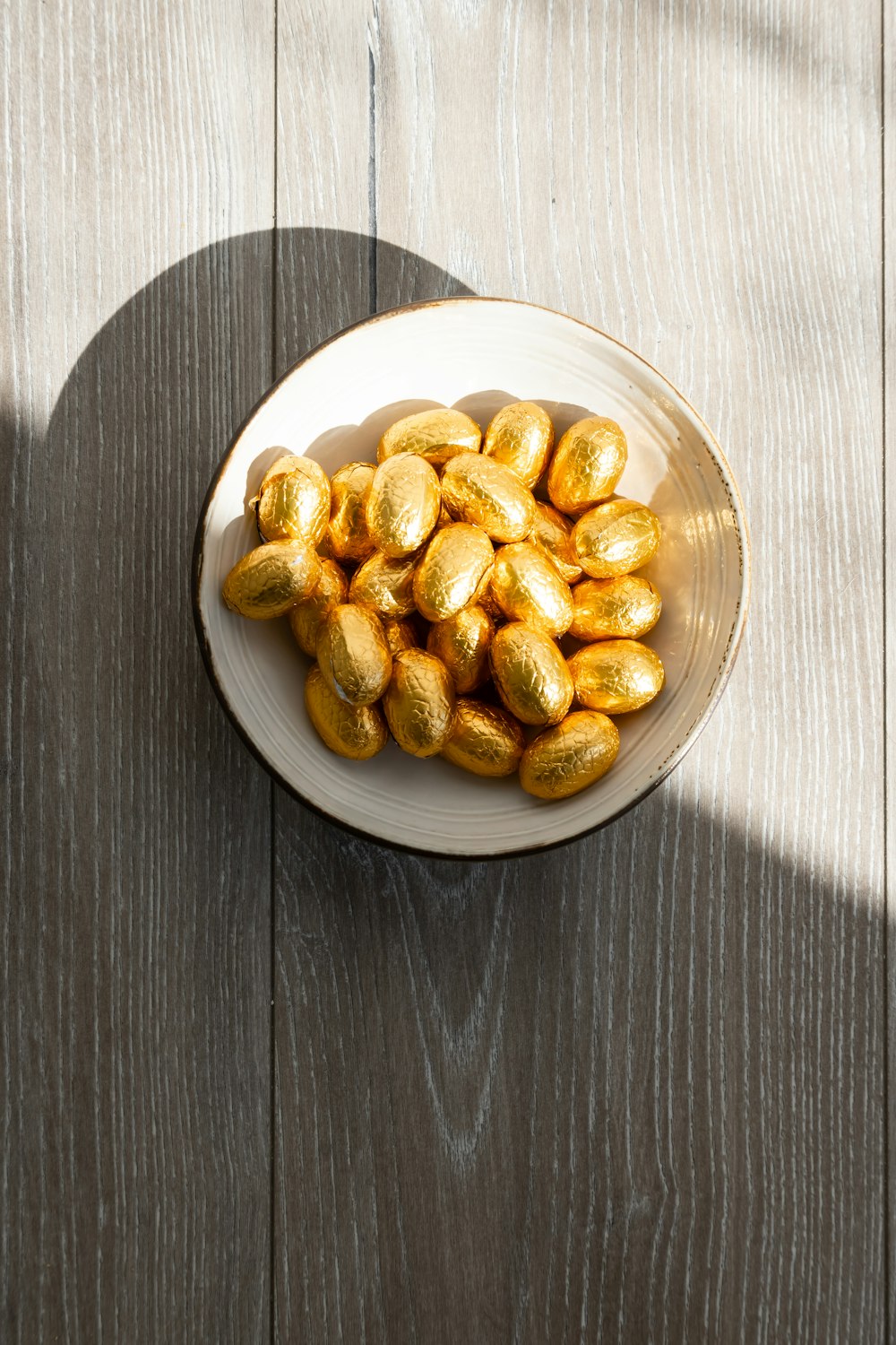 a white bowl filled with gold eggs on top of a wooden table