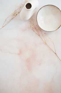 a white table topped with a white bowl and a white vase