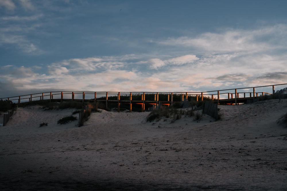 a wooden bridge over a sandy beach under a cloudy sky