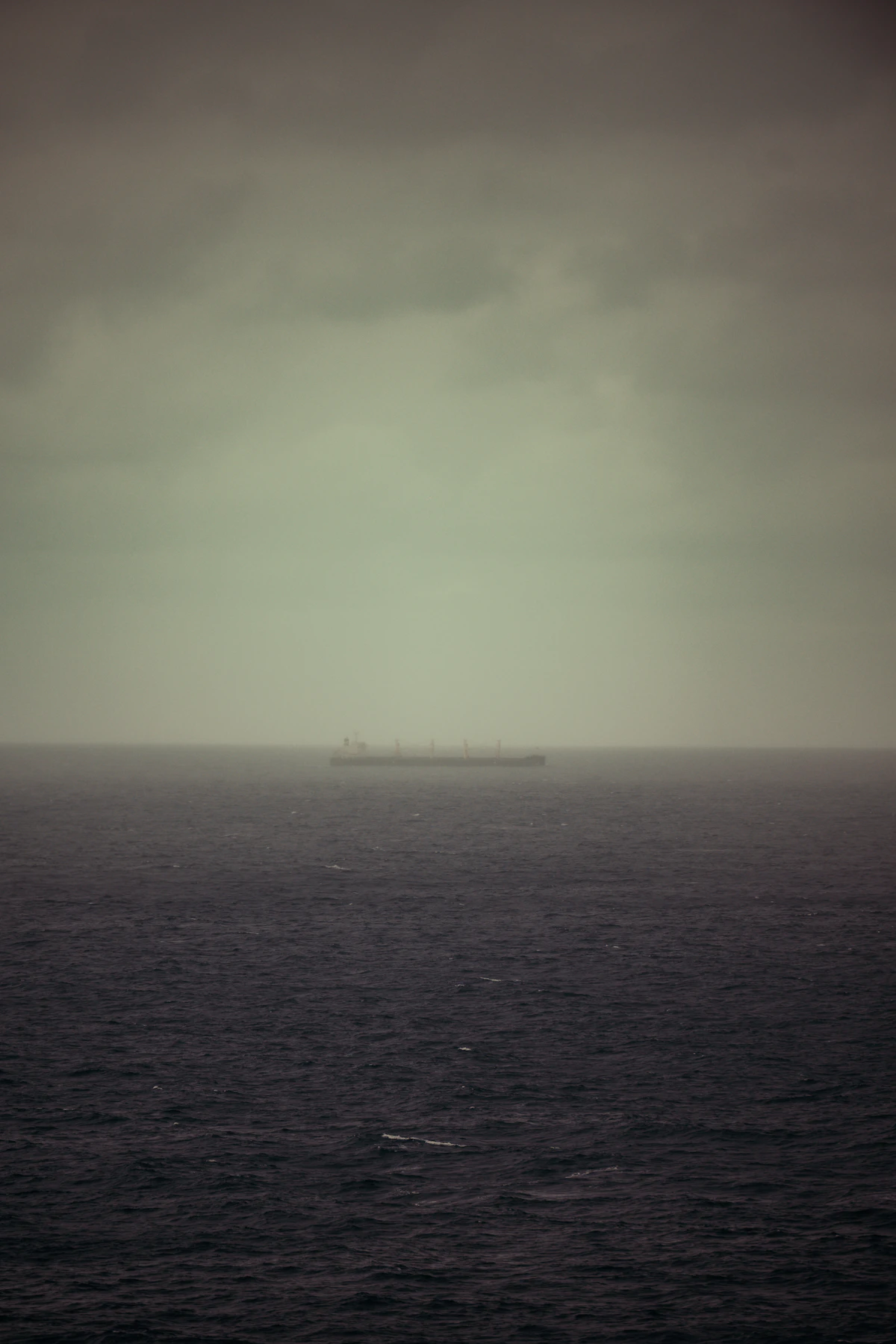 A cruise ship at sea beneath heavy dark storm clouds and rough water