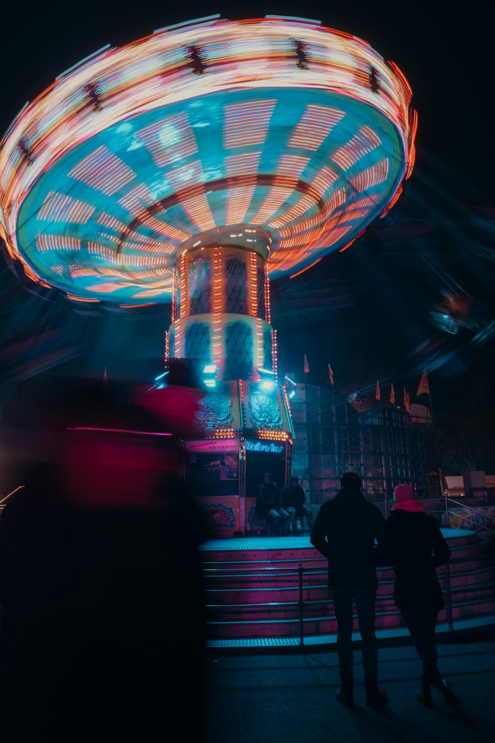personnes debout autour d’un manège de carnaval la nuit