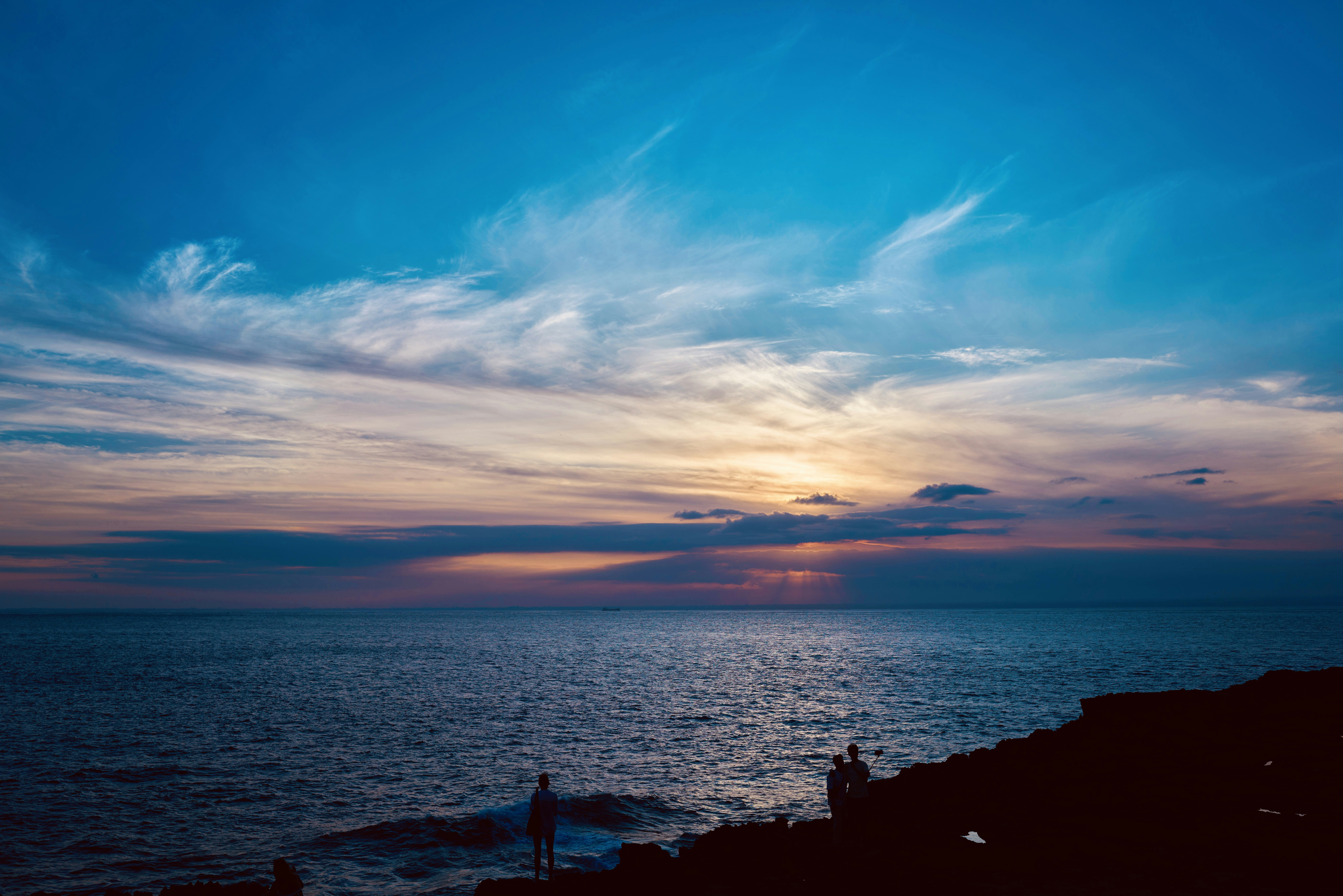 A couple of people standing on top of a cliff near the ocean photo ...
