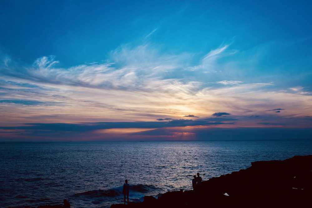 a couple of people standing on top of a cliff near the ocean