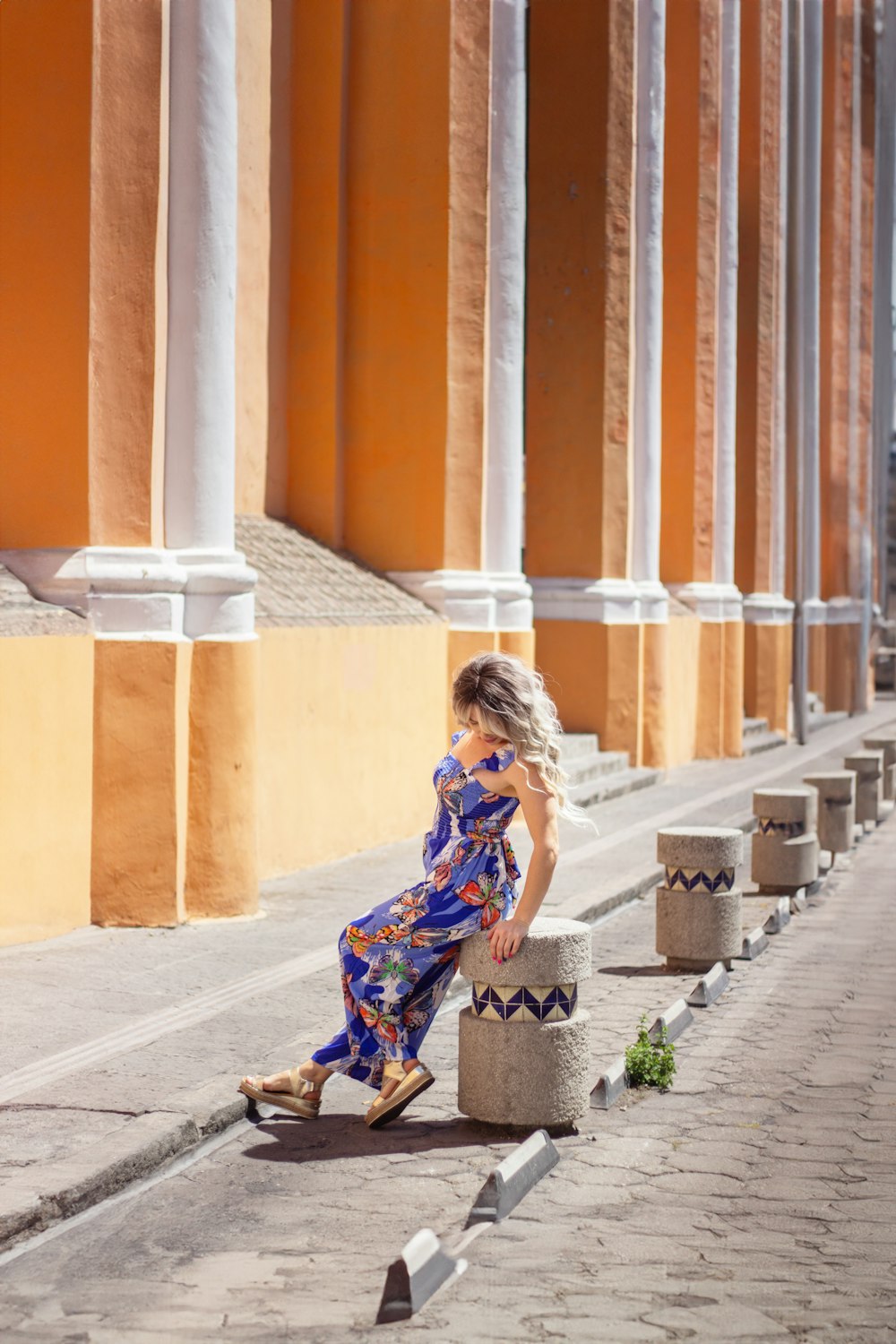 a woman in a blue dress is sitting on a pillar