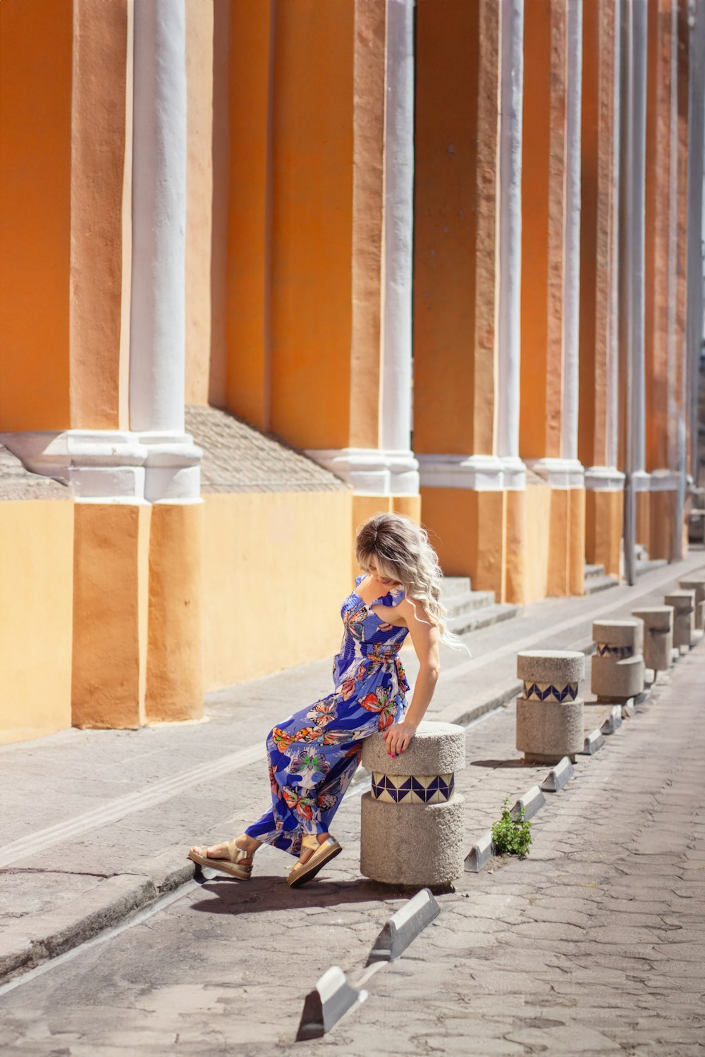 Una donna in un vestito blu è seduta su un pilastro