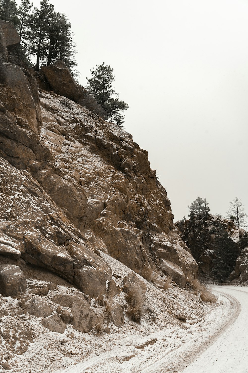 a snow covered road next to a rocky cliff