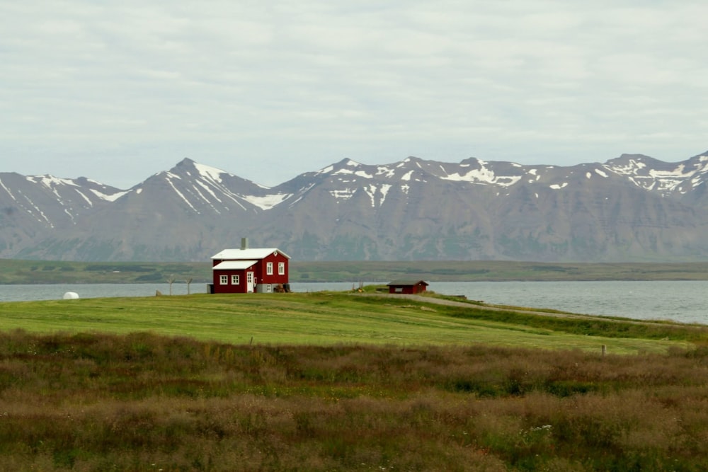 a small red house on a grassy hill next to a body of water