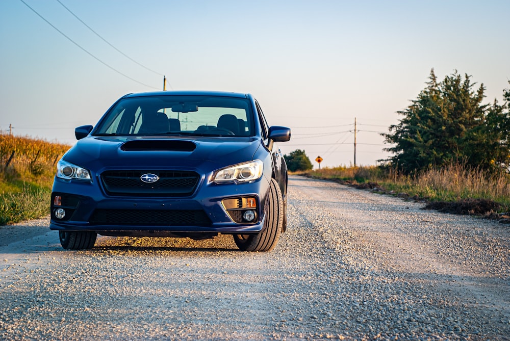 a blue subarunt is parked on a gravel road