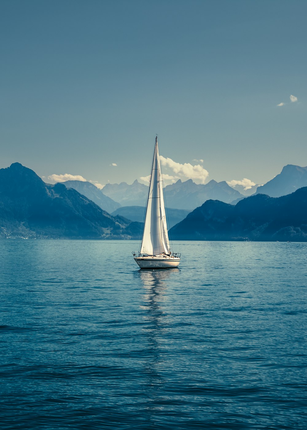 a sailboat in the middle of a lake with mountains in the background