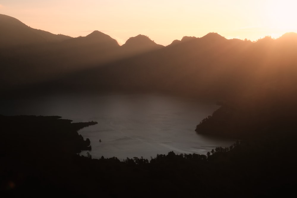 the sun is setting over a lake with mountains in the background