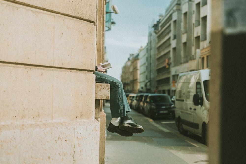 a person sitting on a ledge reading a book