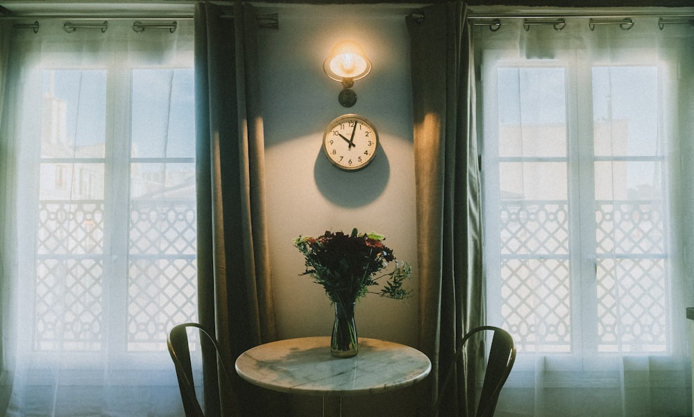 a table with a vase of flowers and a clock on the wall