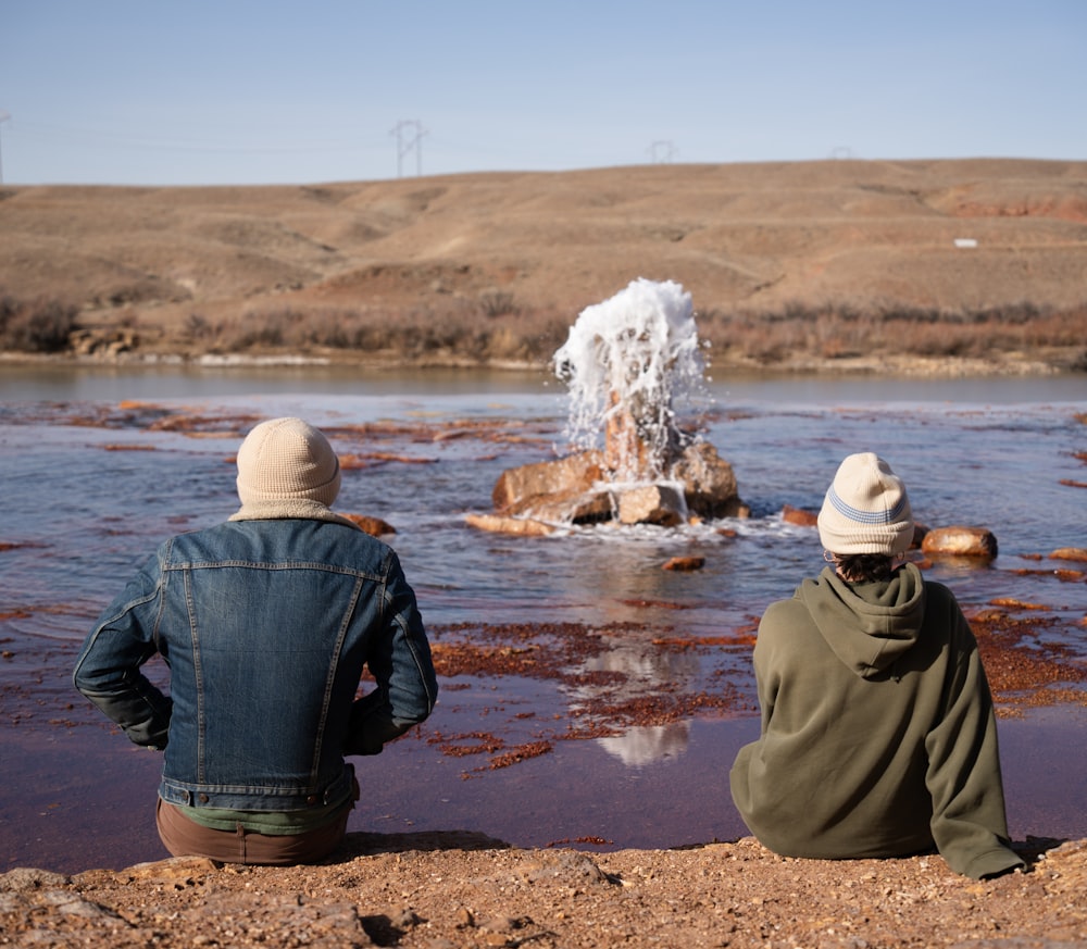 a couple of people sitting on top of a rock near a body of water