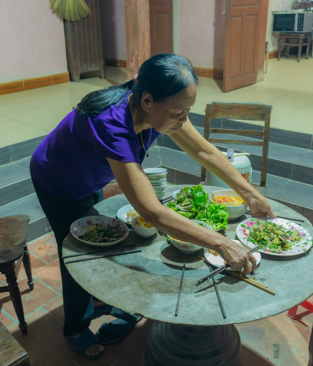 Una mujer con una camisa morada está preparando comida en una mesa
