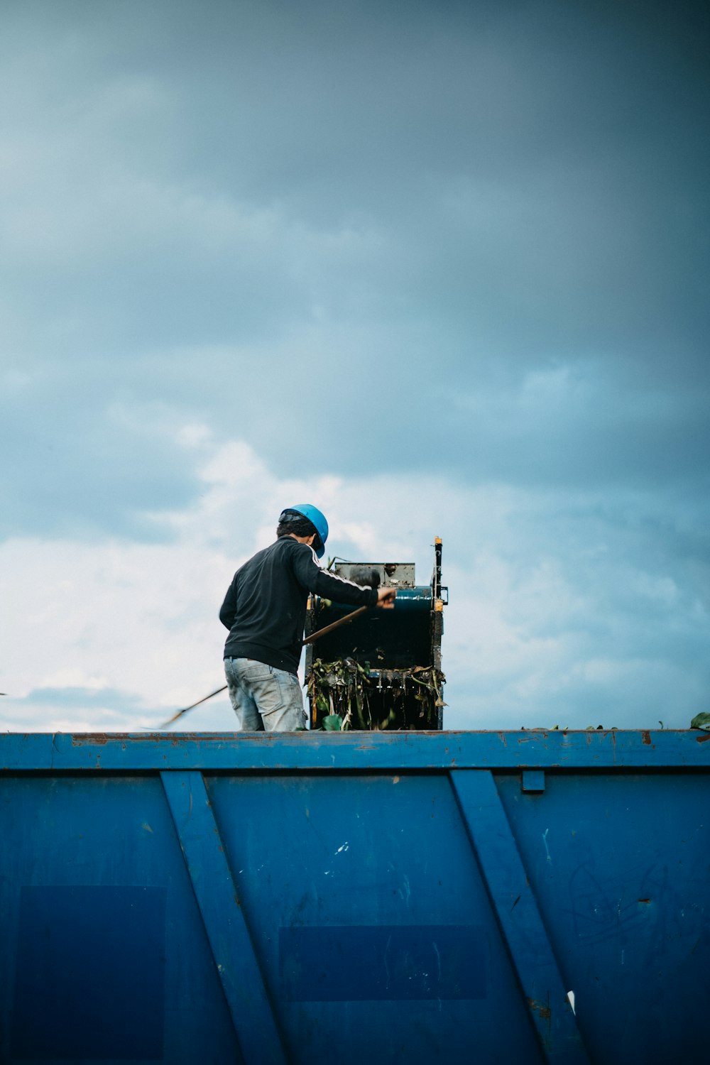 a man standing on top of a blue dumpster