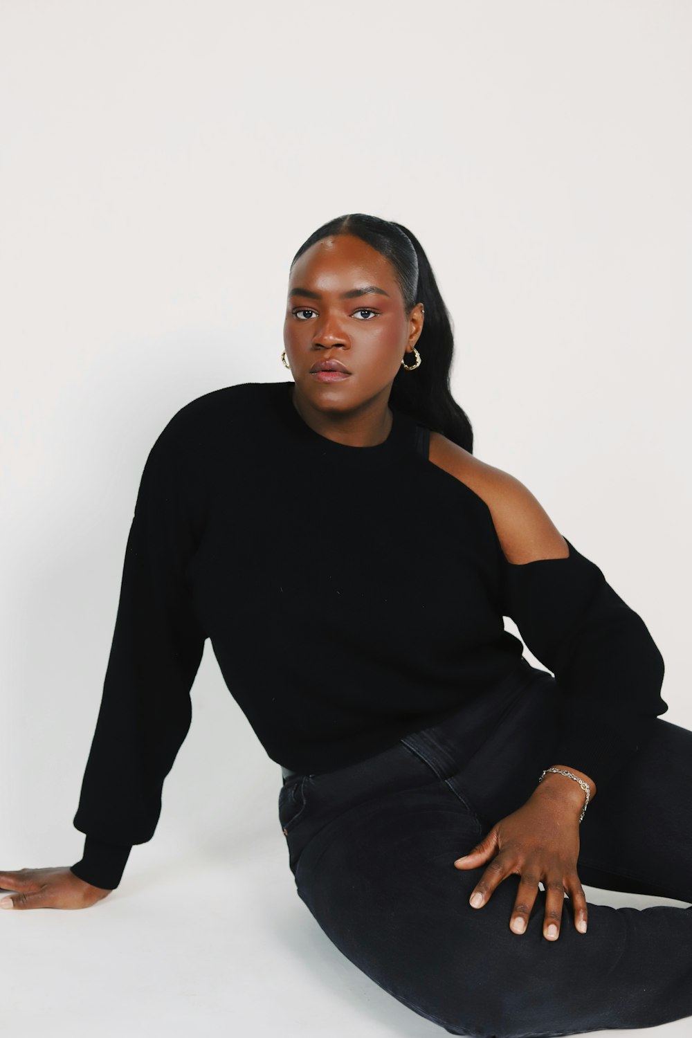 a woman sitting on the ground wearing a black sweater and jeans