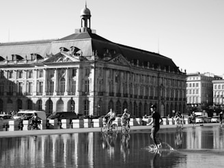 a black and white photo of people riding bikes in front of a building