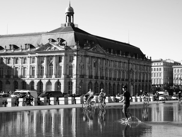 a black and white photo of people riding bikes in front of a building