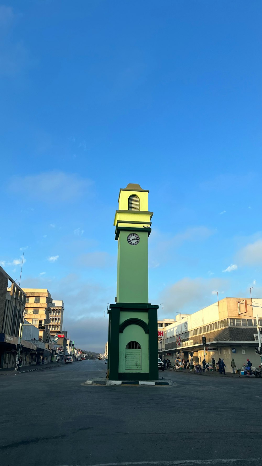 a green and yellow clock tower in the middle of a street
