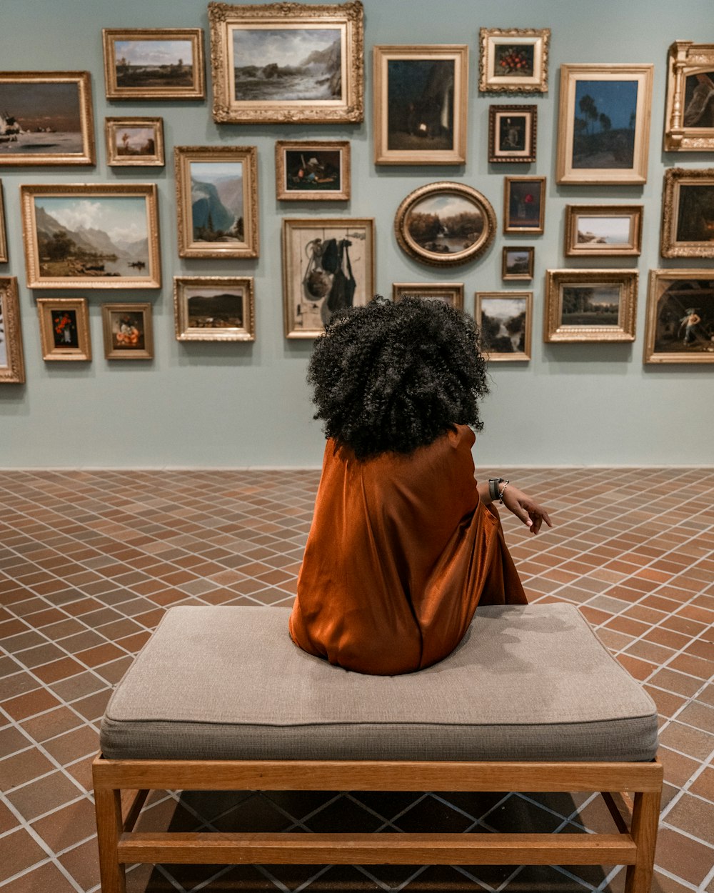 a woman sitting on a bench in front of a wall of pictures