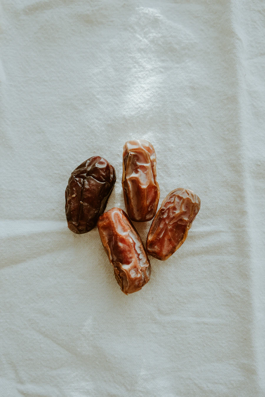 Four large, glossy dates laid out on a cream linen cloth