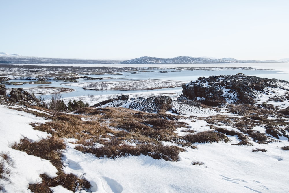 a snow covered field with a lake in the distance