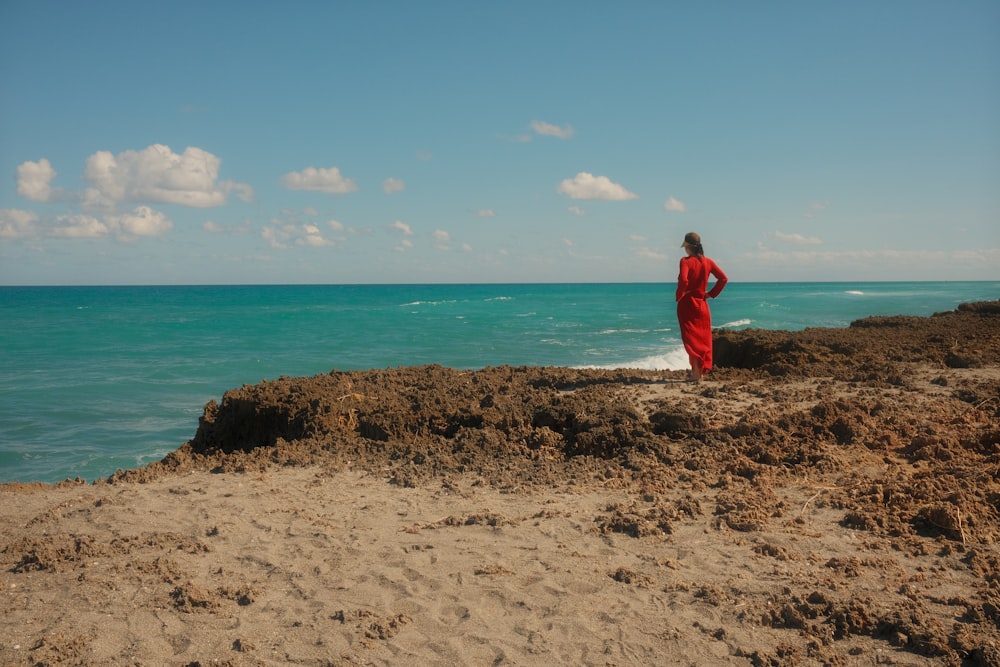 uma pessoa com um manto vermelho em pé em uma praia