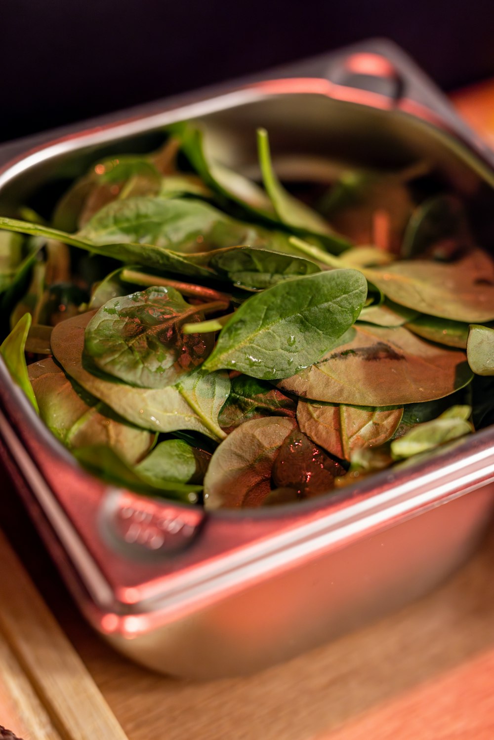 a metal container filled with green vegetables on top of a wooden table