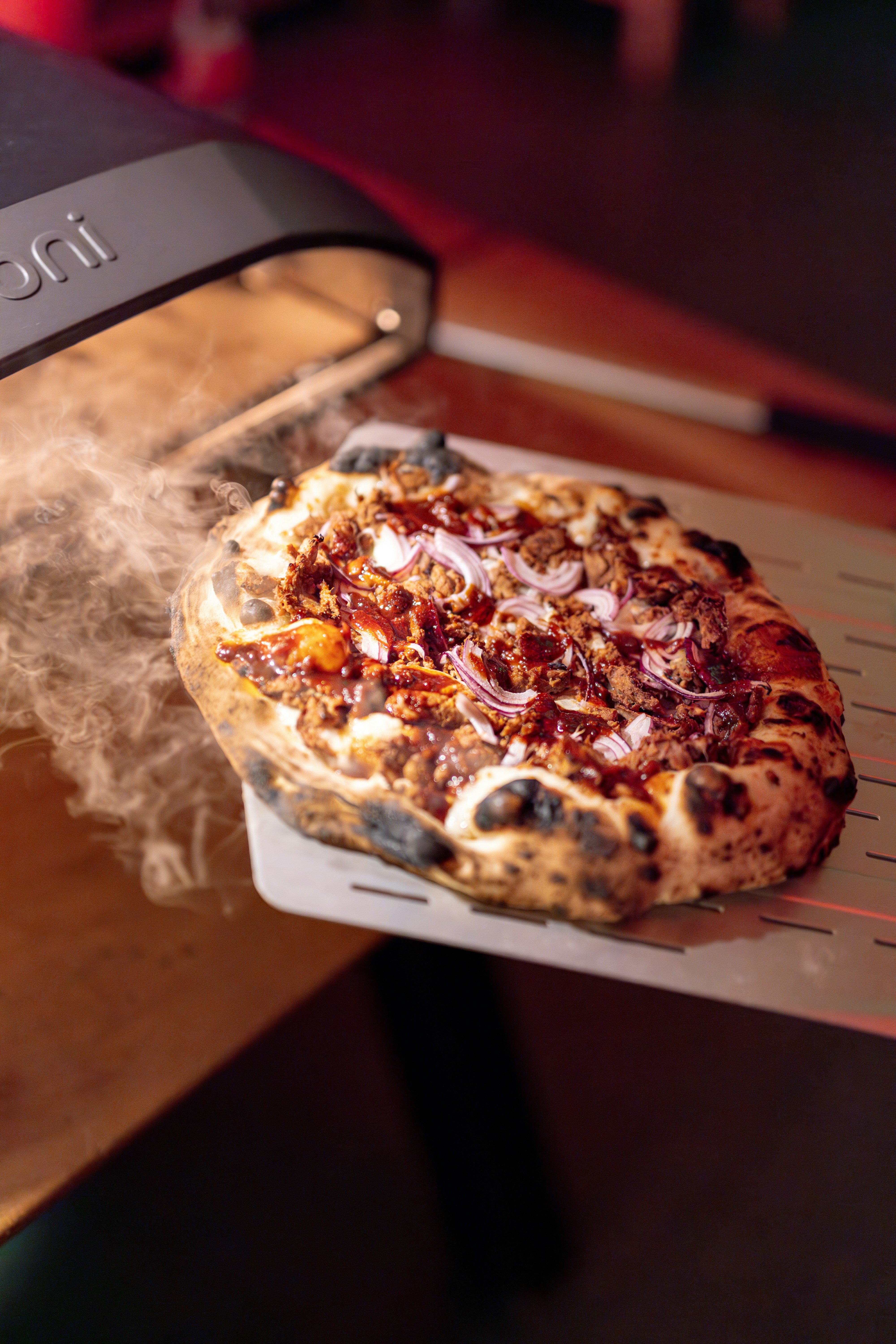 Uno chef fa scivolare una pizza con carne dal forno.