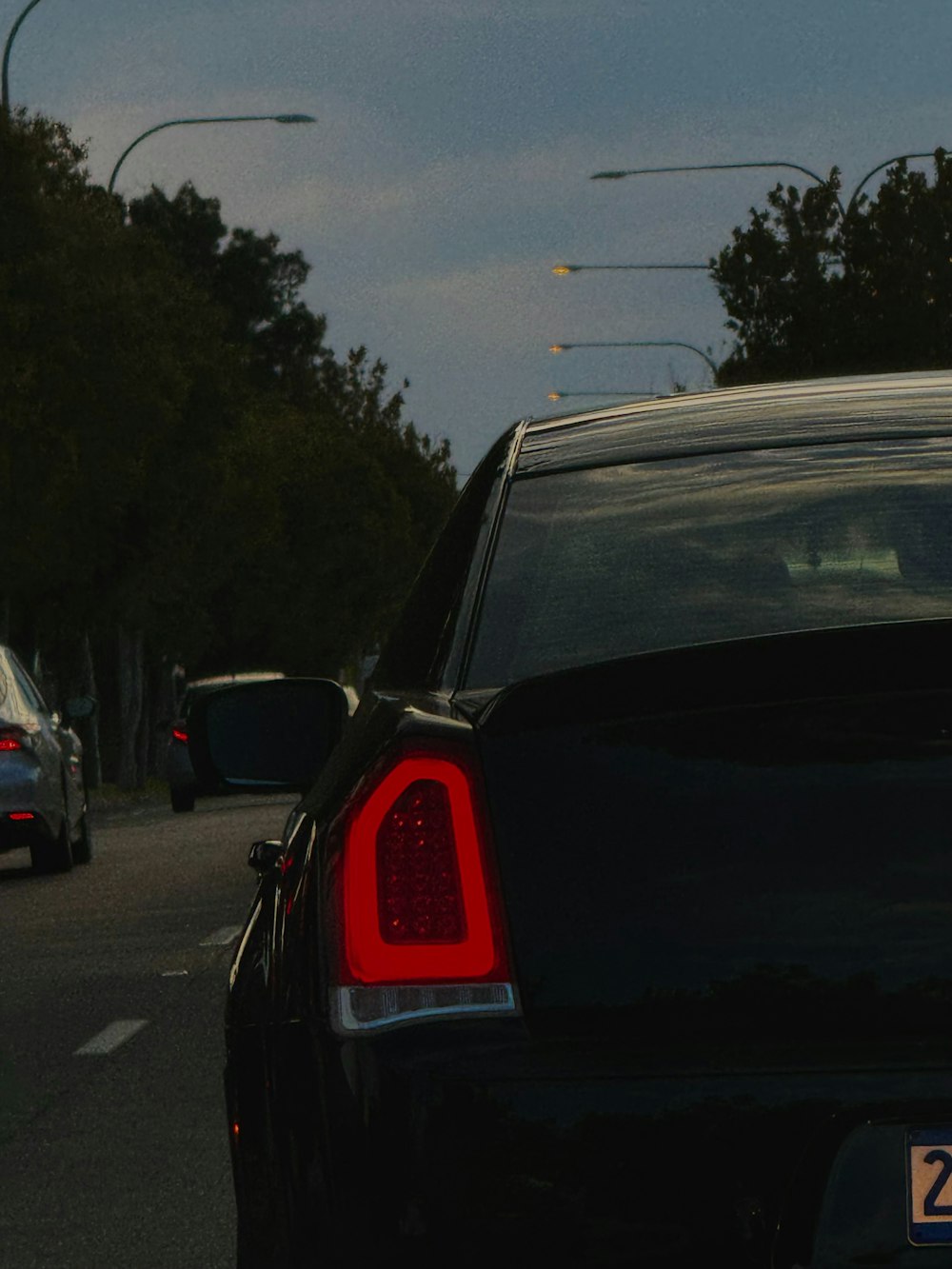 a black car driving down a street next to a forest