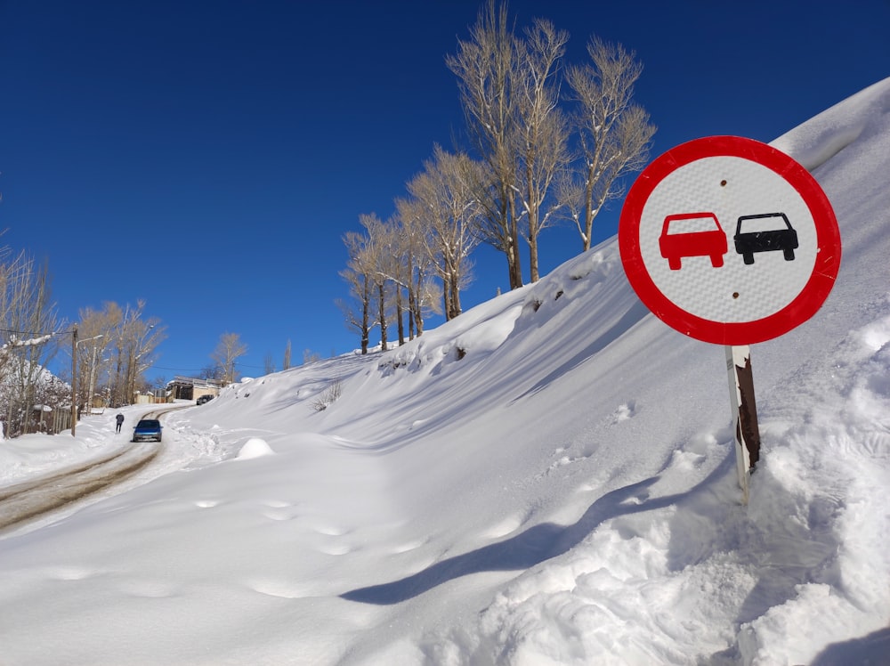 a red and white sign sitting on the side of a snow covered road