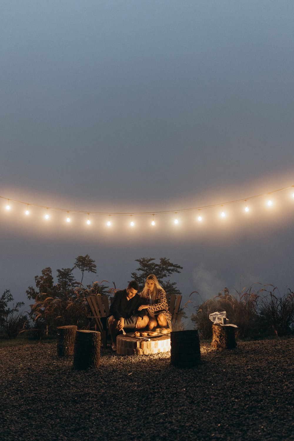 two people sitting on a bench in front of a string of lights