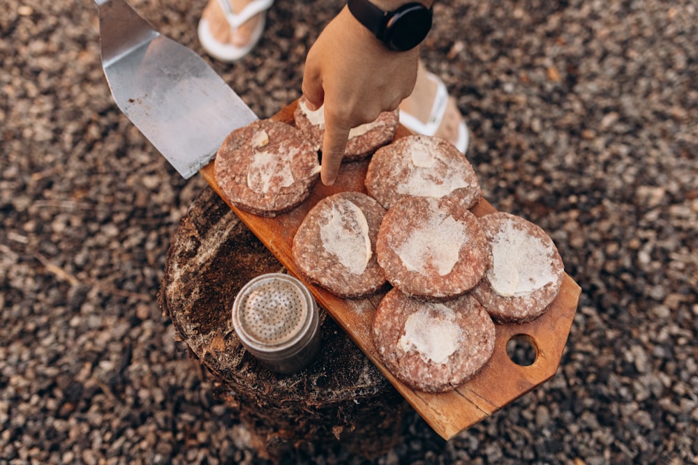 a person holding a knife over a tray of powdered donuts