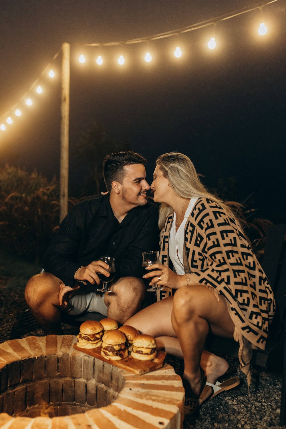 a man and woman sitting on a bench next to a fire pit
