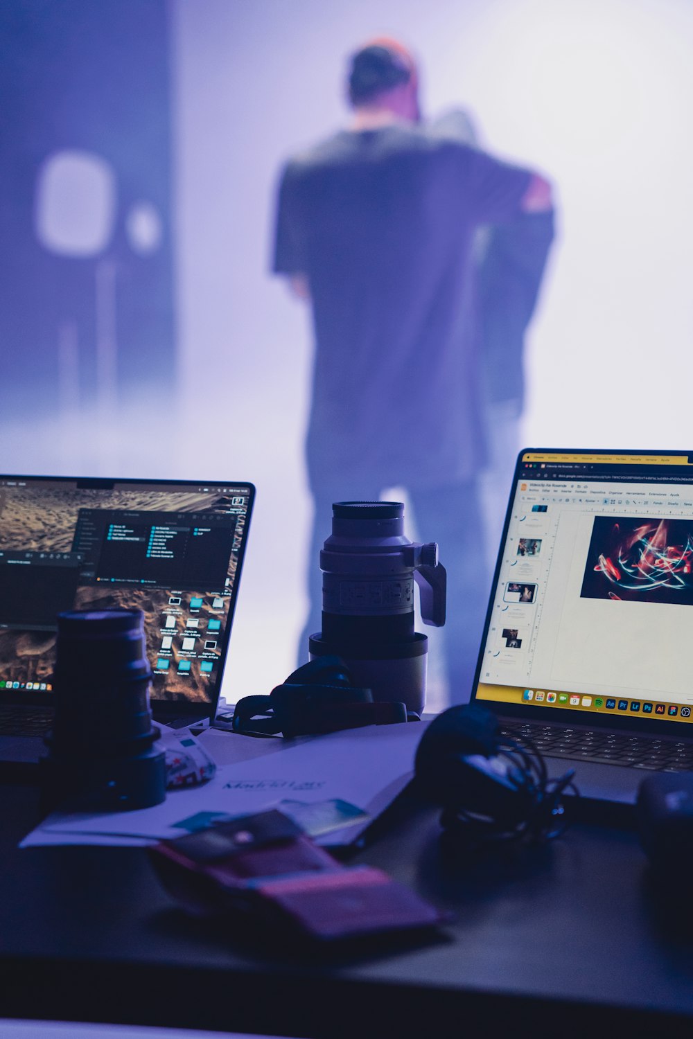 two laptops sitting on a desk with a man in the background