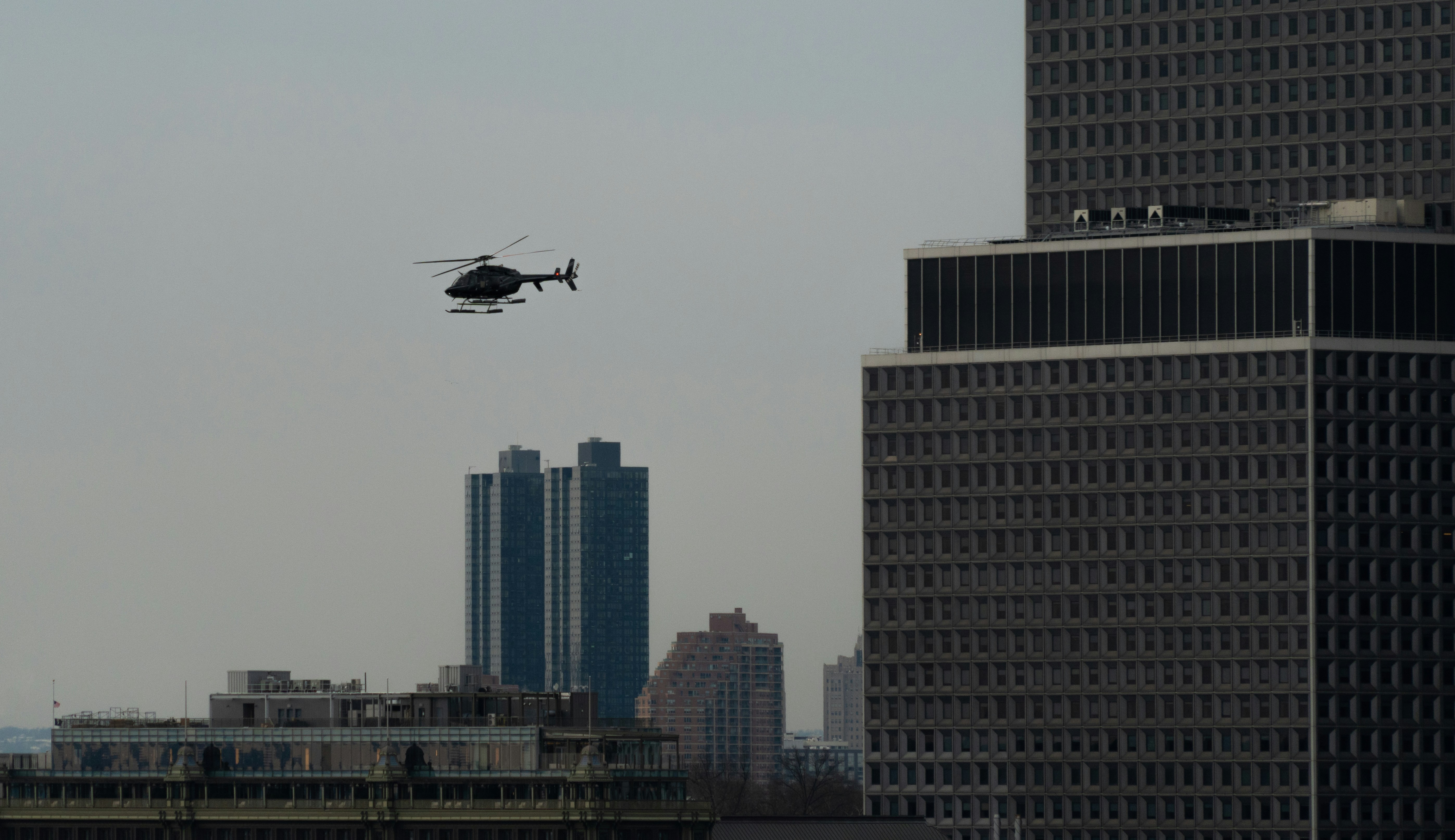 a helicopter flying over a city with tall buildings, 