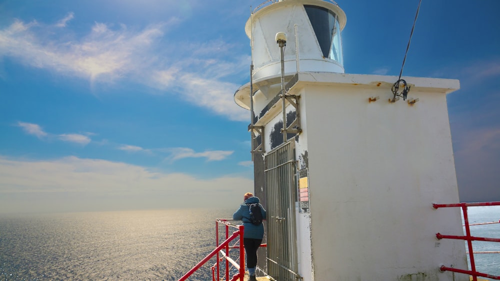a person standing on a red railing near a white lighthouse