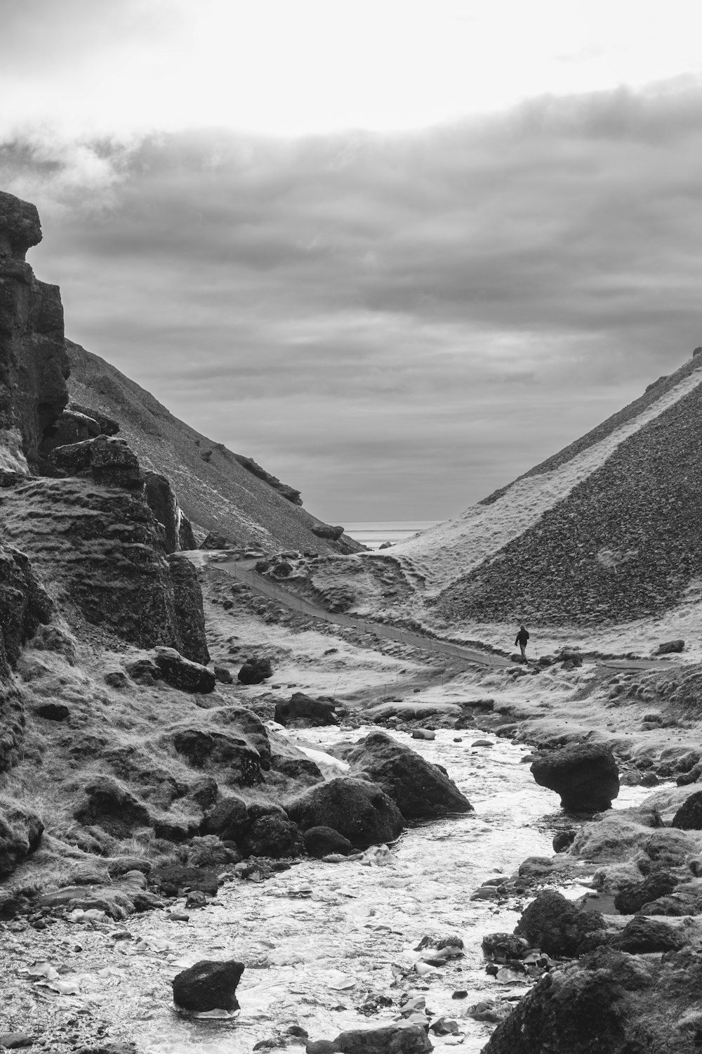 a black and white photo of a man walking on a rocky path