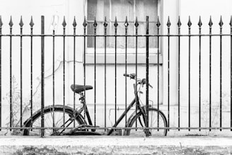 a bicycle parked next to a fence in front of a building